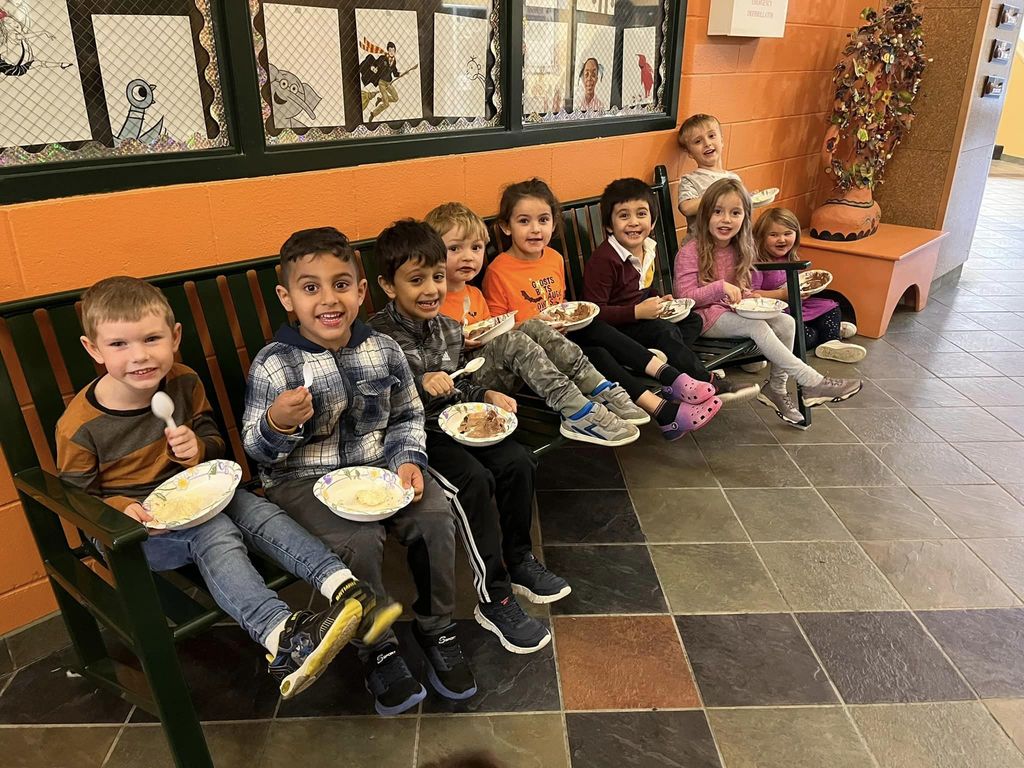 Kindergarteners sitting on a bench eating bowls of ice cream and smiling