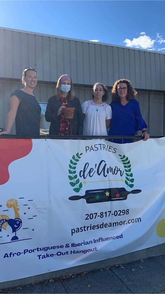 Four women standing, one holding a check, behind the Pastries de’Amor sign