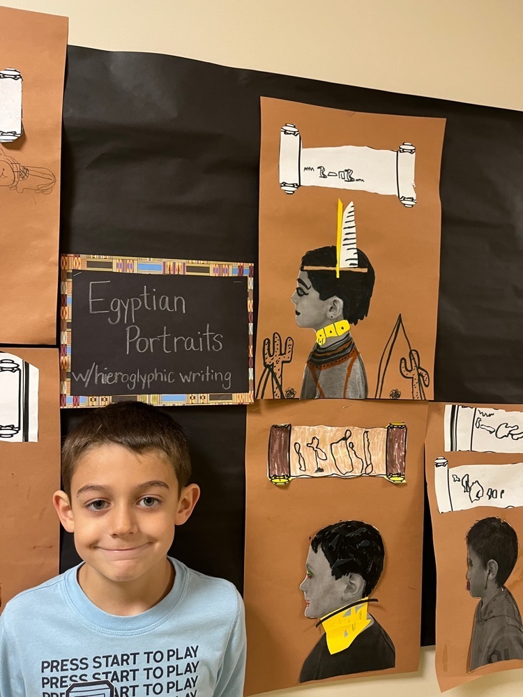 student poses next to their Egyptian style self portrait profile and name in hieroglyphs 