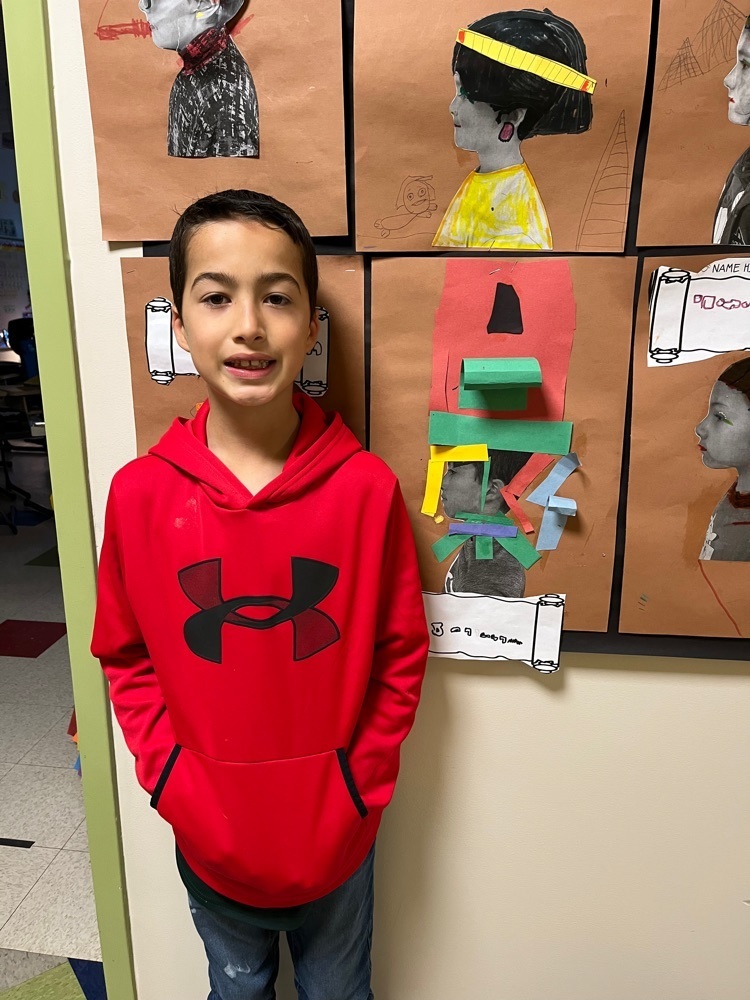 student poses next to their Egyptian style self portrait profile and name in hieroglyphs