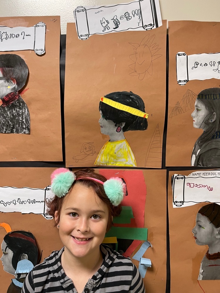 student poses next to their Egyptian style self portrait profile and name in hieroglyphs 