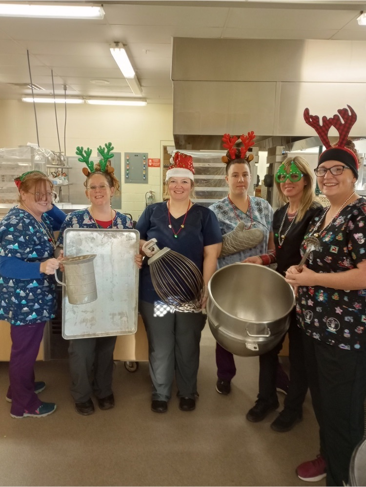 six kitchen staff holding kitchen tools and wearing antlers and holiday decorations