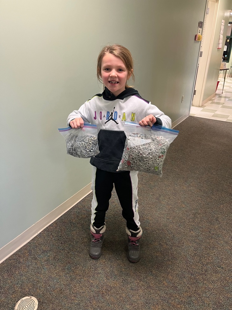 first grade girl holding two gallon bags of can tabs