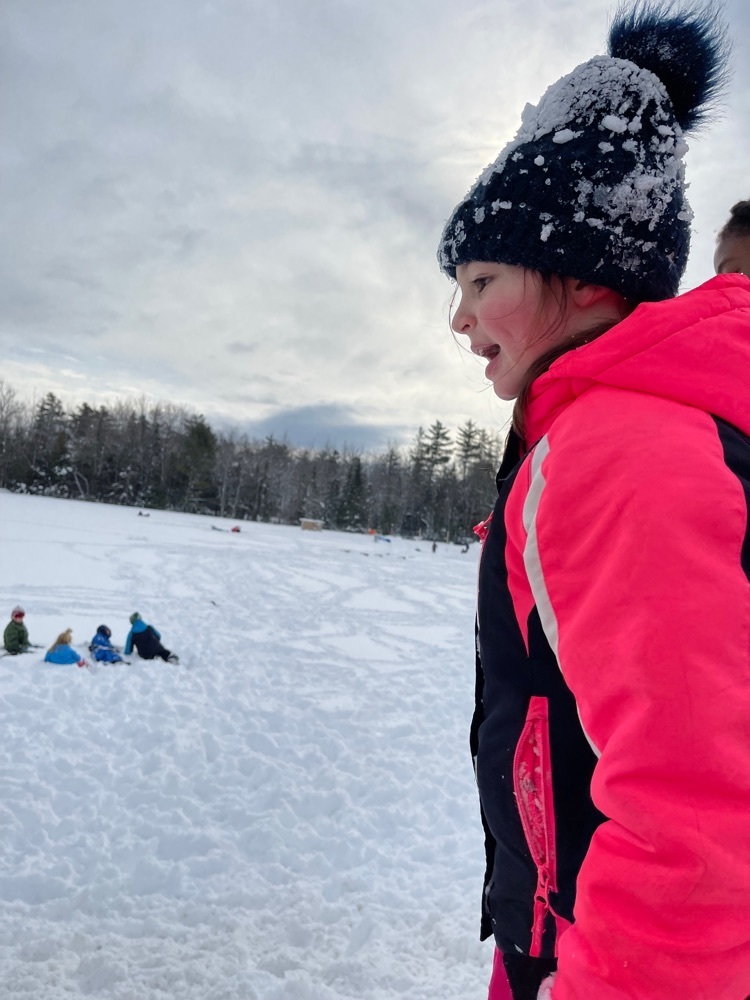 student in snow gear with others playing in a snowy field in the background