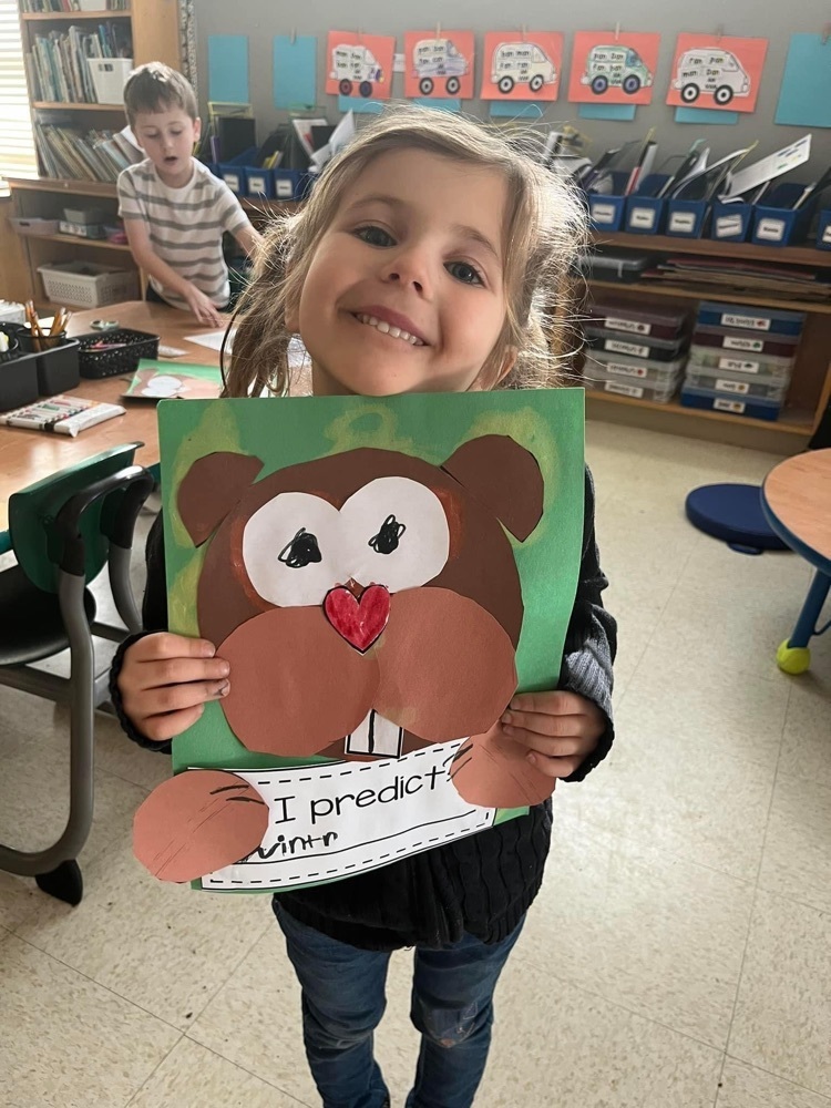 kindergarten student holds up their construction paper groundhog and prediction