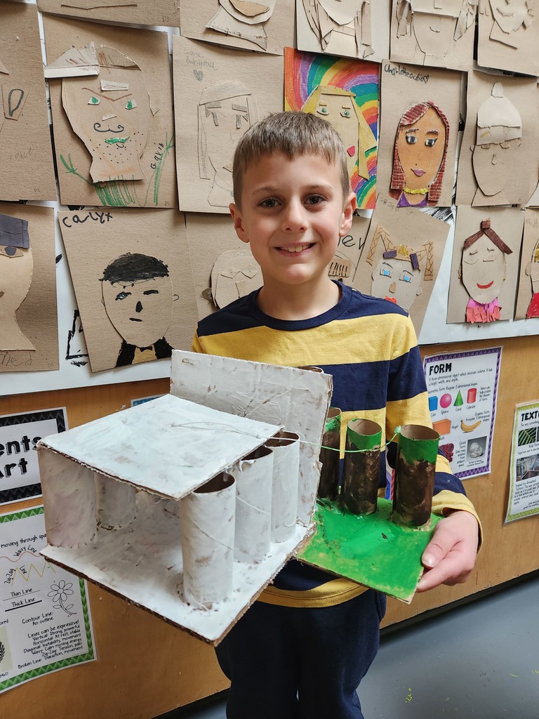 Second grader holding cardboard and wire sculpture of the White House and trees