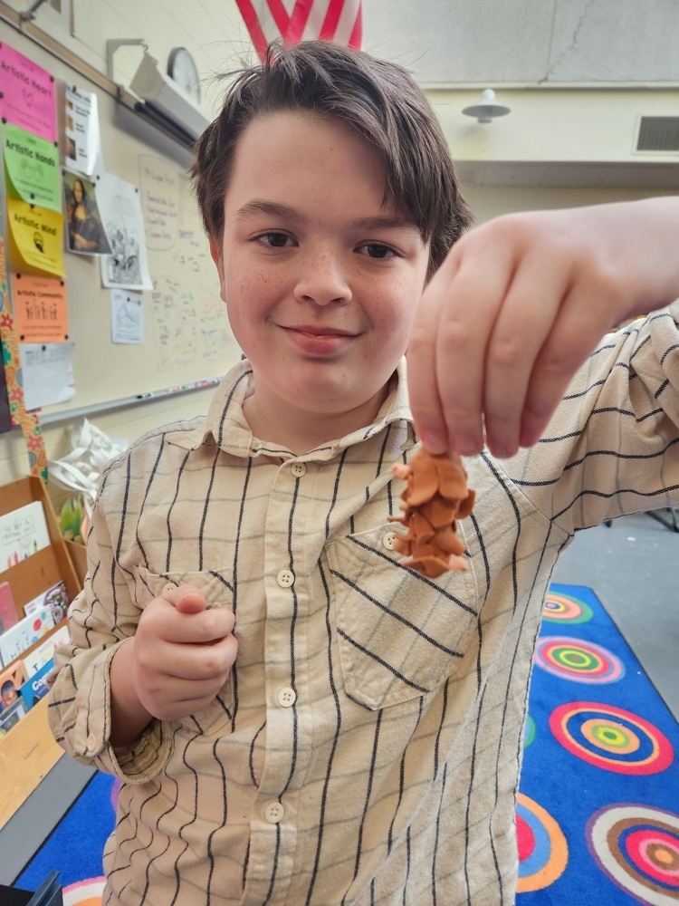 fourth grade boy holding a pine cone he made of clay